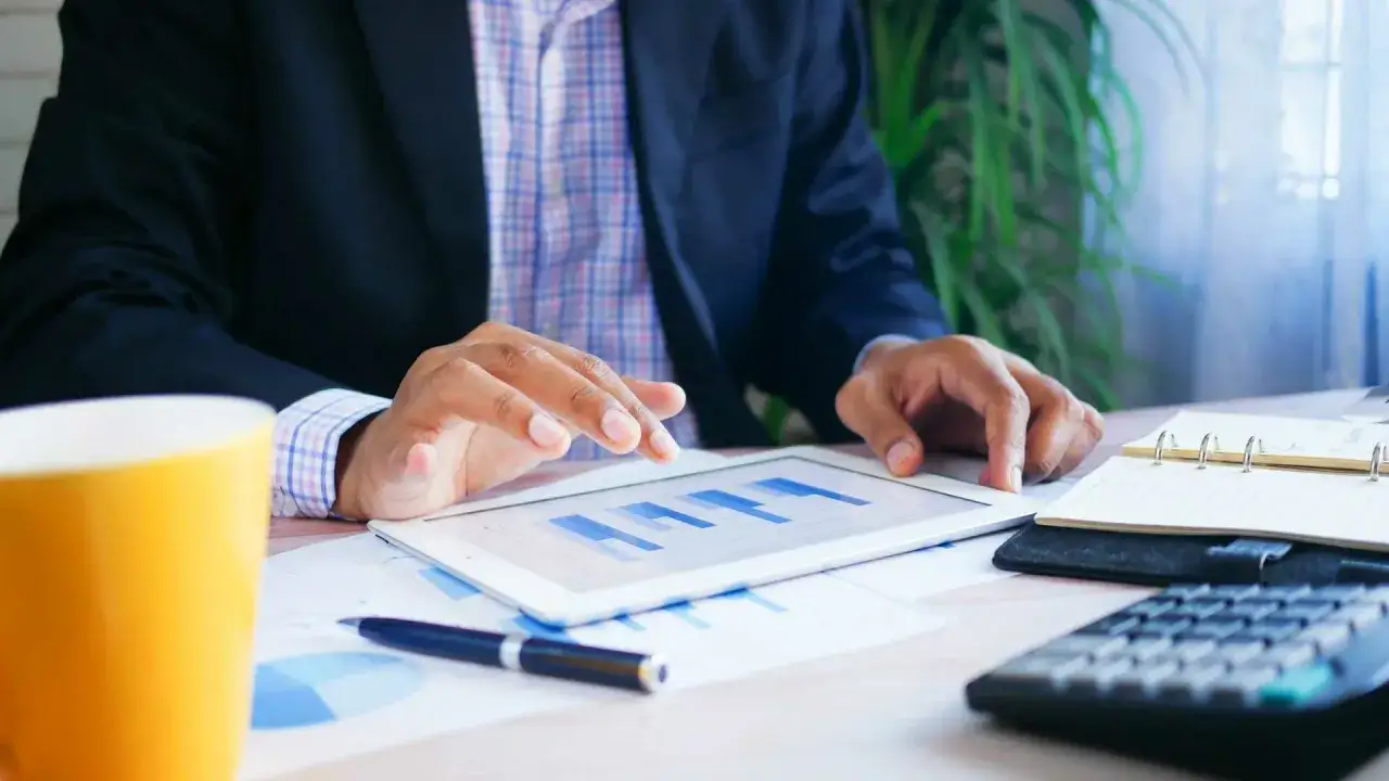 Mężczyzna analizuje wykresy na tablecie, by sprawdzić, jak można wziąć coś na raty. Obok leży kalkulator i notatnik.