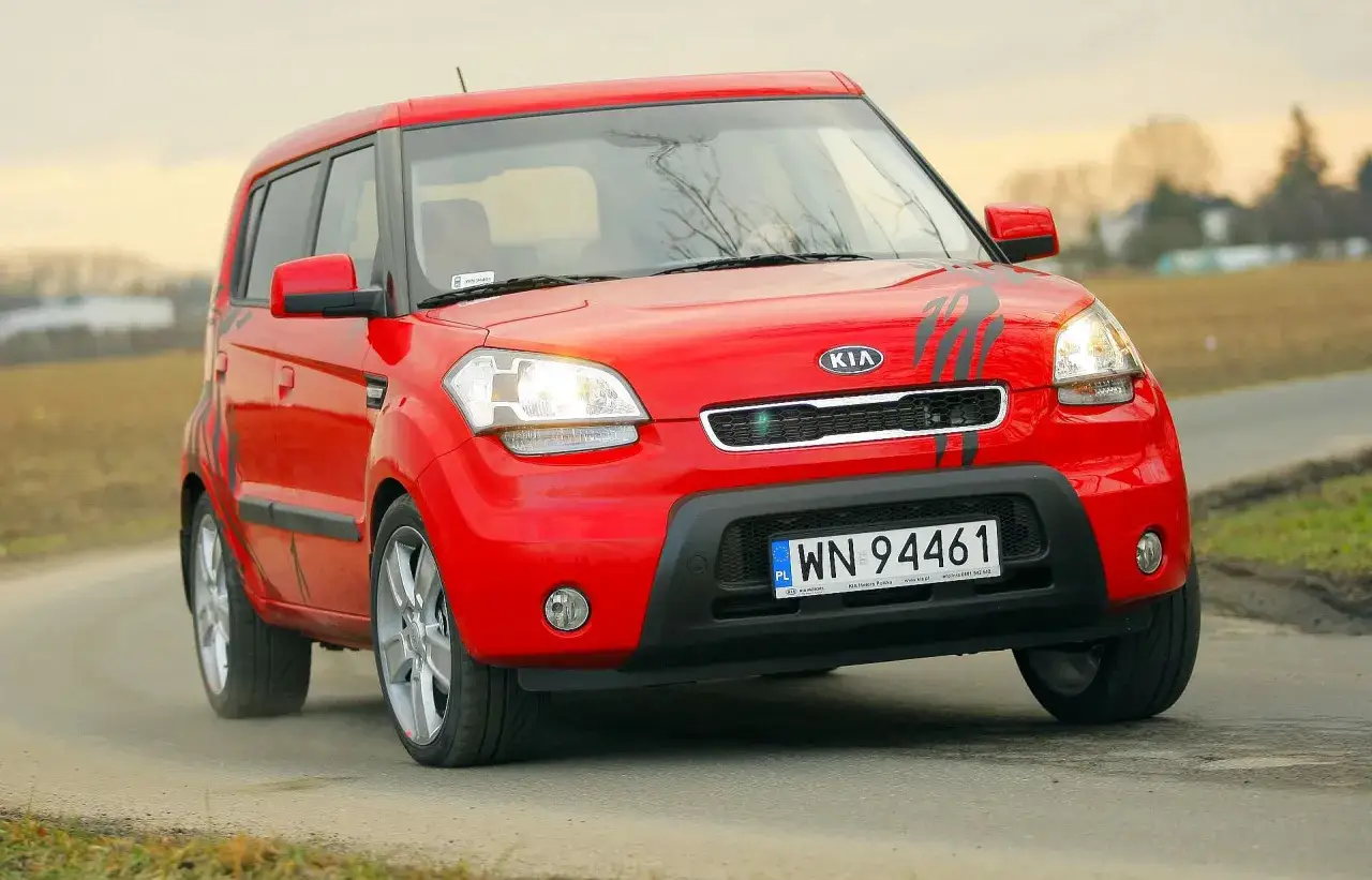 Czerwony Kia Soul z czarnymi pasami na masce jedzie po drodze.
