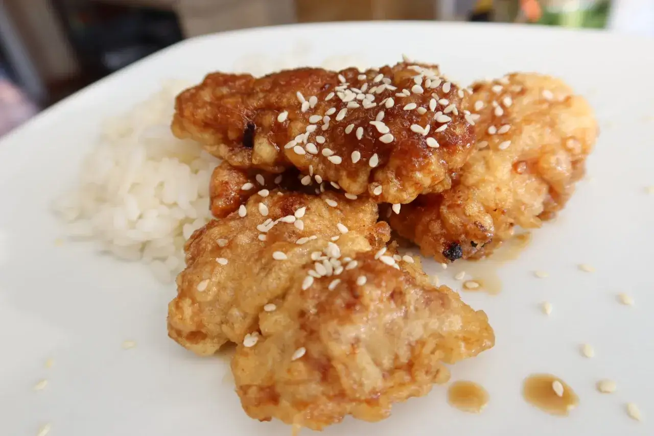 Azjatycki kurczak generała Tso w zdrowej wersji z pieca, polany sosem i posypany sezamem, podany z ryżem.