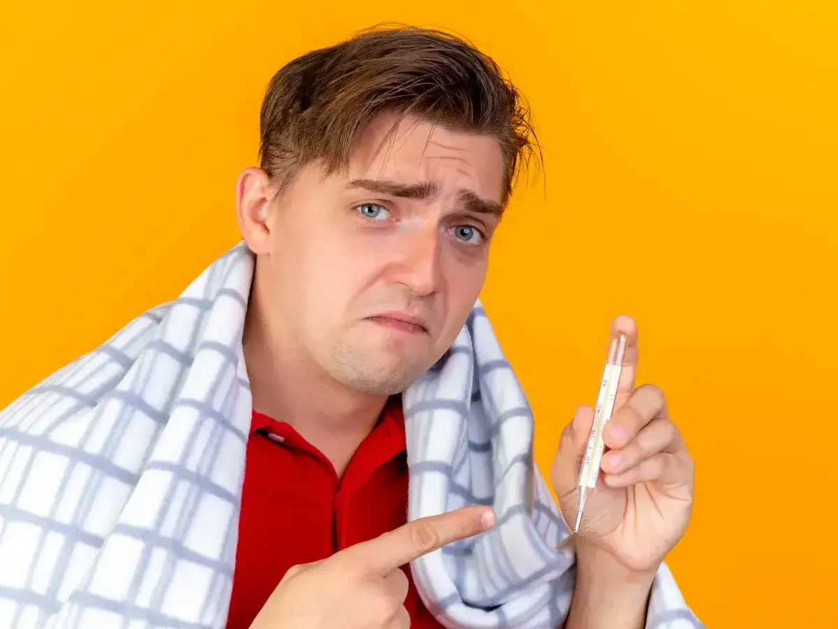 Chory mężczyzna z termometrem w dłoni, zastanawia się, od jakiej temperatury zbijać gorączkę u dorosłego.