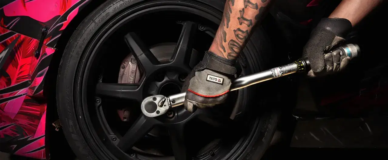 Ręka w rękawicy dokręca kluczem dynamometrycznym śruby koła. Precyzyjny moment dokręcania kół tabela pomaga w prawidłowym montażu.