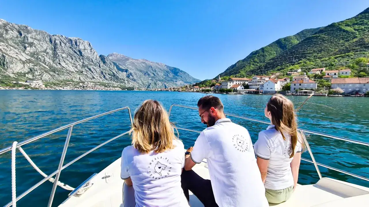 Trzy osoby na łodzi podziwiają zatokę w Czarnog&oacute;rze. Widok potwierdza, że czarnog&oacute;ra jest bezpieczna i piękna.
