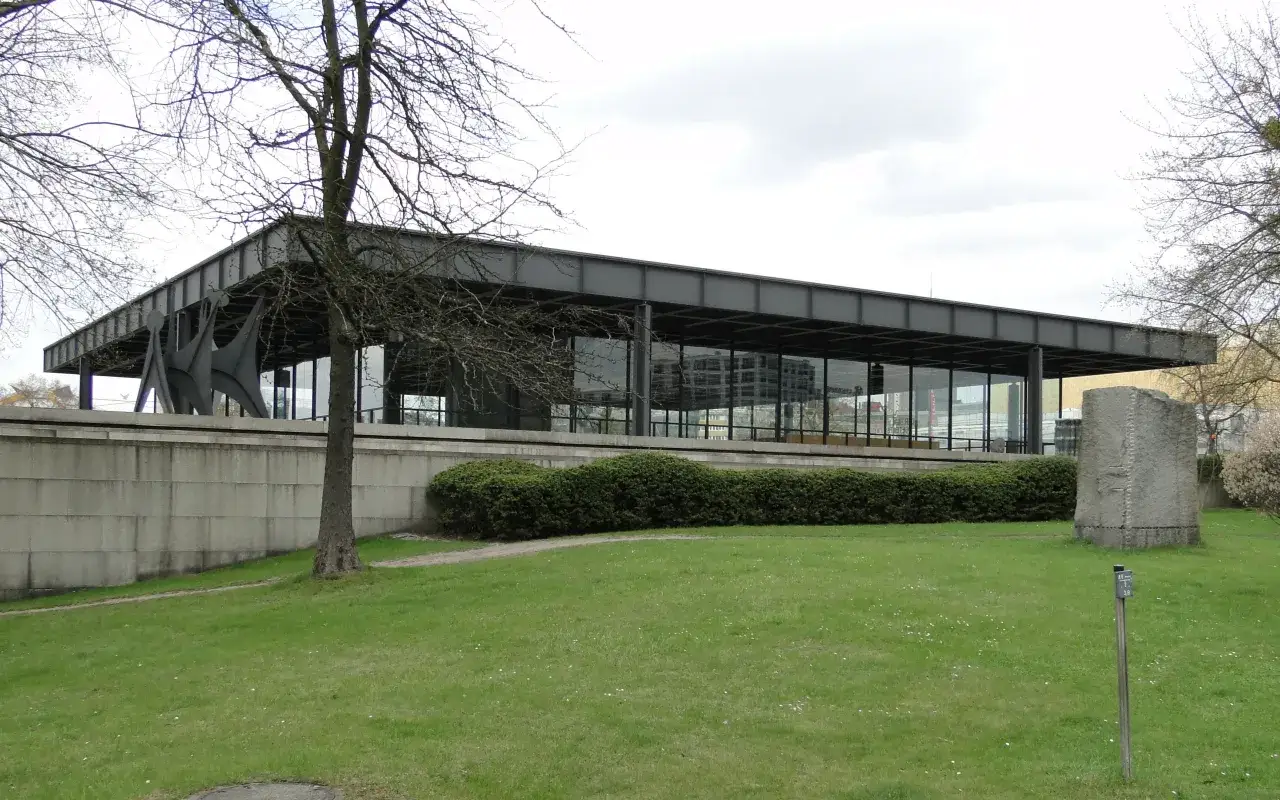 Nowoczesna architektura muzeum sztuki nowoczesnej w Berlinie, z przeszklonymi ścianami i stalową konstrukcją, otoczona zielenią i rzeźbami.