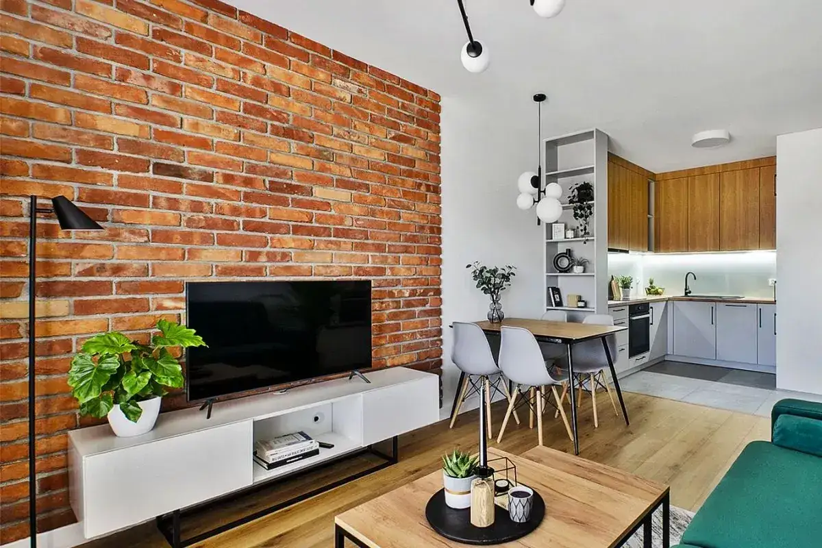 Nowoczesny salon z ceglaną ścianą, jadalnią i aneksem kuchennym. Zastanawiasz się, ile jest warte mieszkanie w bloku z takim wnętrzem?