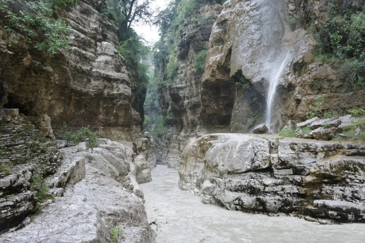 Wodospad w malowniczym kanionie w Albanii, gdzie rzeka płynie między stromymi, skalnymi ścianami porośniętymi zielenią.
