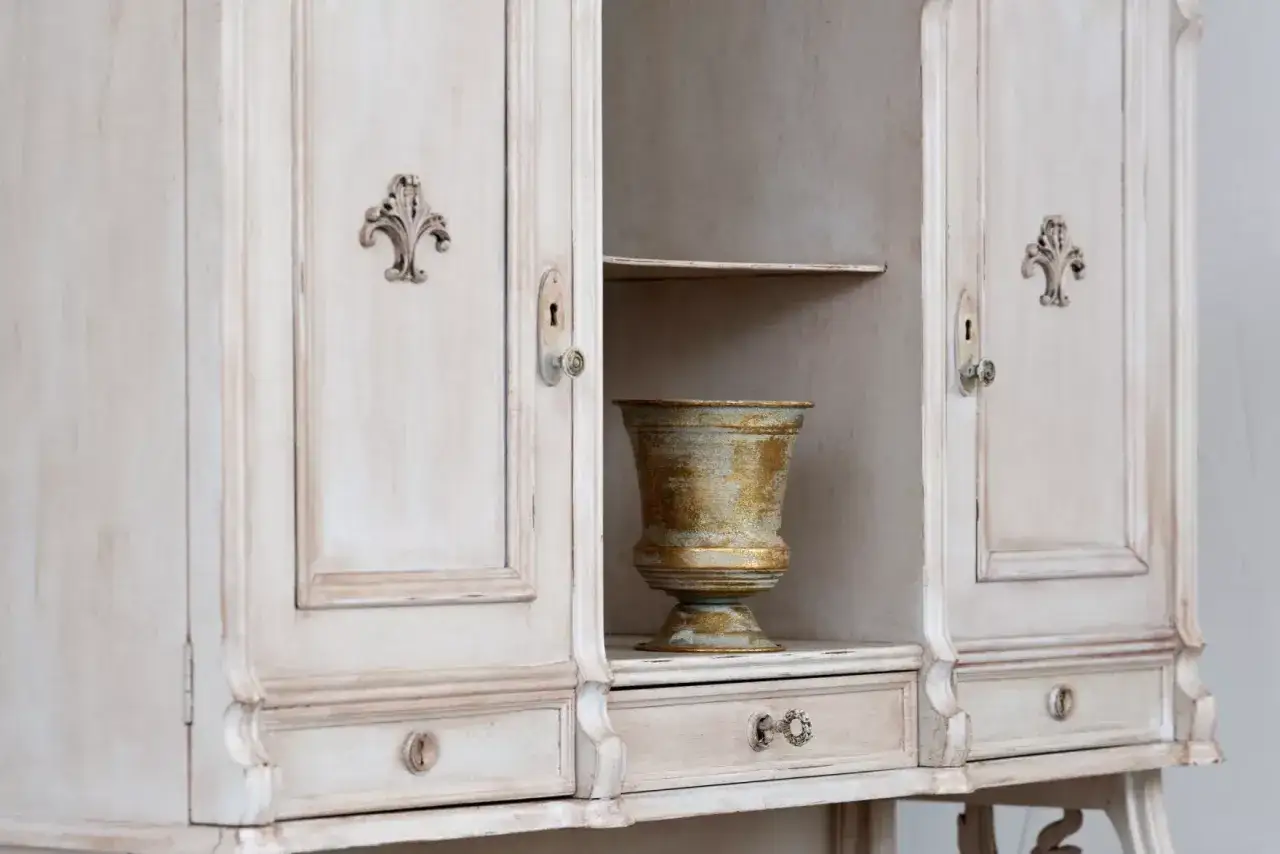 Odnowione meble sosnowe w stylu shabby chic, z ozdobnymi uchwytami i złotą wazą.