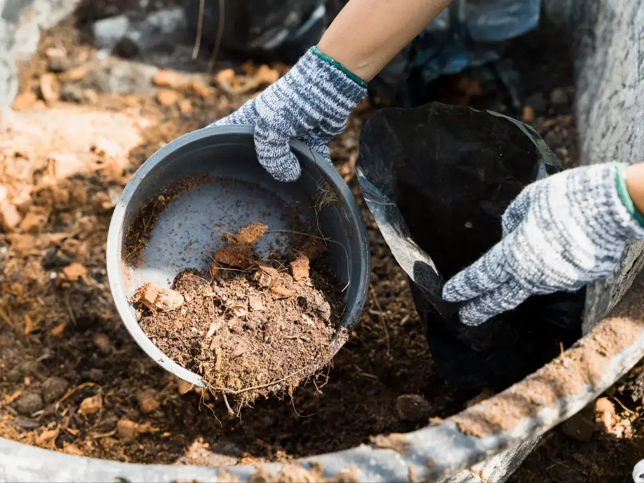 Ręce w rękawiczkach dodają ziemi do kompostownika, co pomoże przyspieszyć kompostowanie.