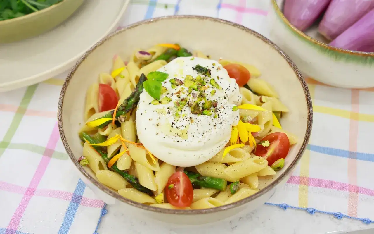 Penne z burratą, szparagami i pomidorkami koktajlowymi, posypane pistacjami. Pyszny makaron ze szparagami w letnim wydaniu.