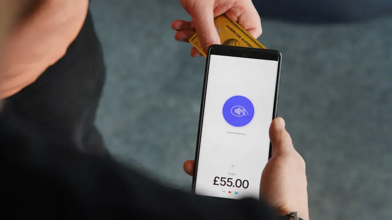 Zbliżenie na płatność zbliżeniową NFC. Karta American Express zbliża się do ekranu telefonu z ikoną płatności.