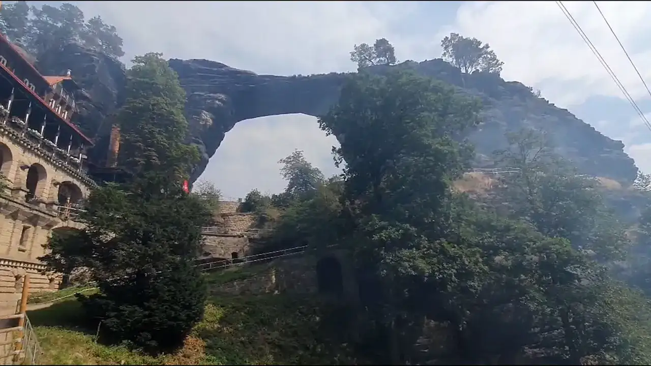 Imponująca kamienna brama w Czechach, z widocznym budynkiem na skale i bujną zielenią.