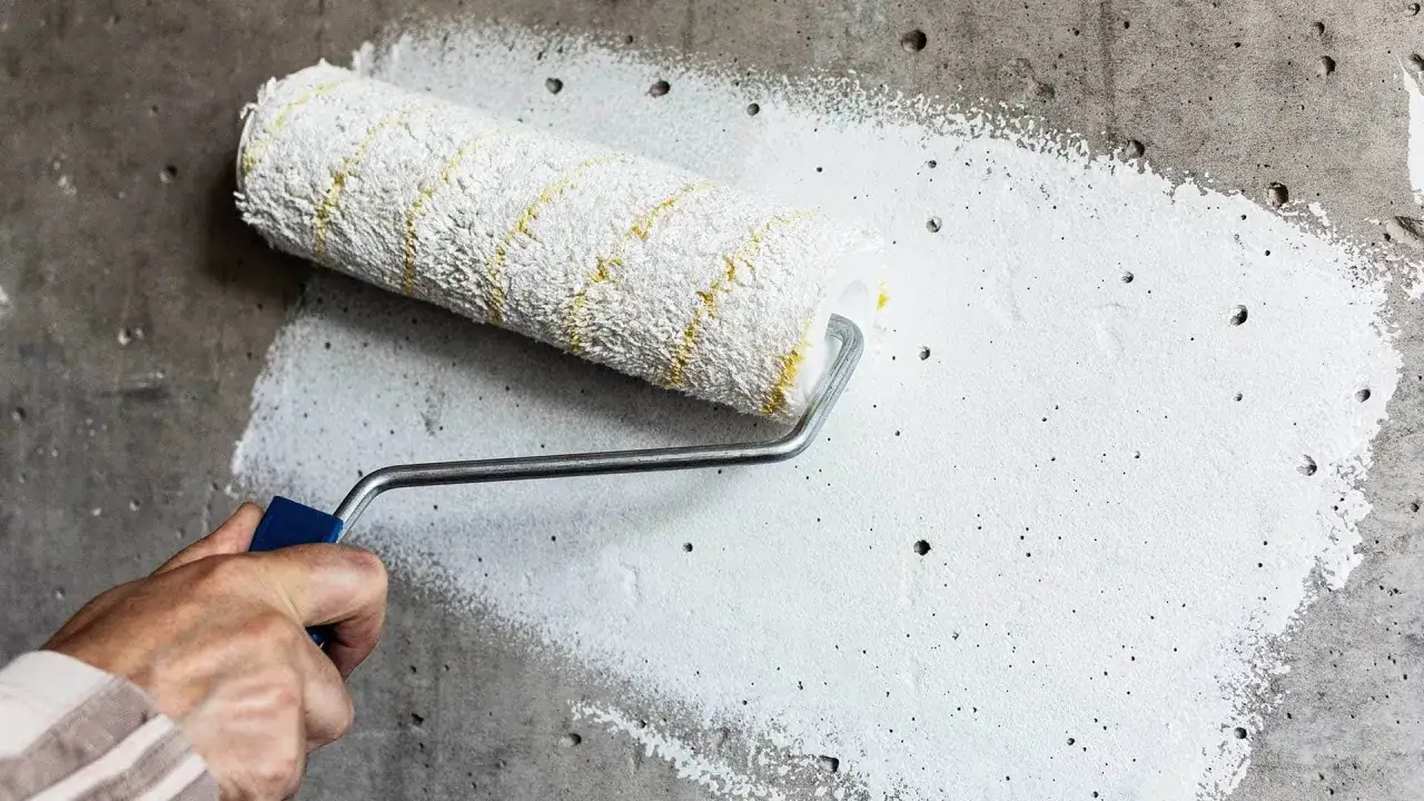 Nakładanie wałkiem białego gruntu pod gładź na betonową ścianę. Przygotowanie powierzchni do dalszych prac wykończeniowych.