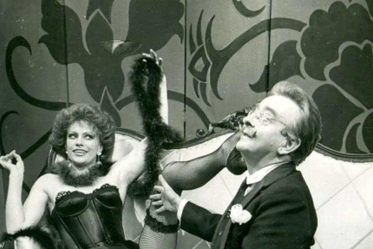 Uśmiechnięta kobieta w czarnym gorsecie i mężczyzna w garniturze, jak żołnierz królowej Madagaskaru, na tle scenografii.