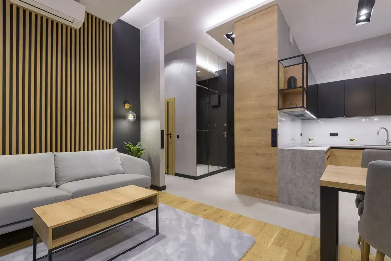 Nowoczesny salon z szarą kanapą i stolikiem kawowym. Ściana za kanapą ozdobiona jest pionowymi lamelami, kt&oacute;re dodają wnętrzu ciepła i stylu.