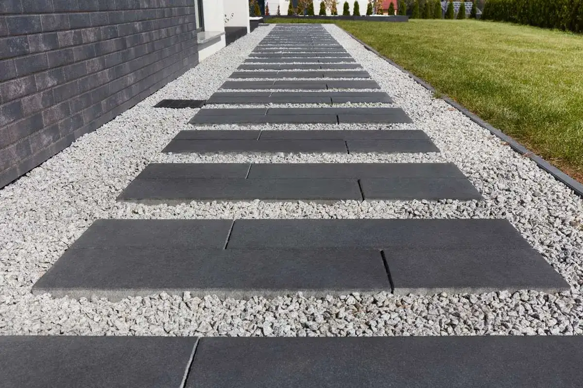 Nowoczesna ścieżka z prostokątnych płyt i białego żwiru wokół domu. Kostka brukowa wokół domu zdjecia prezentuje eleganckie wykończenie.
