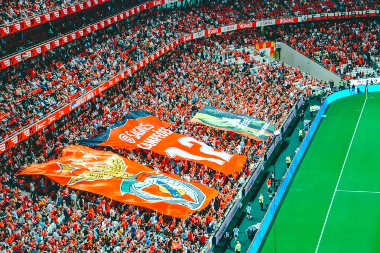 Tryumfujący kibice klubu piłkarskiego z Lizbony, trzymający wielkie flagi z herbem i numerem 12.