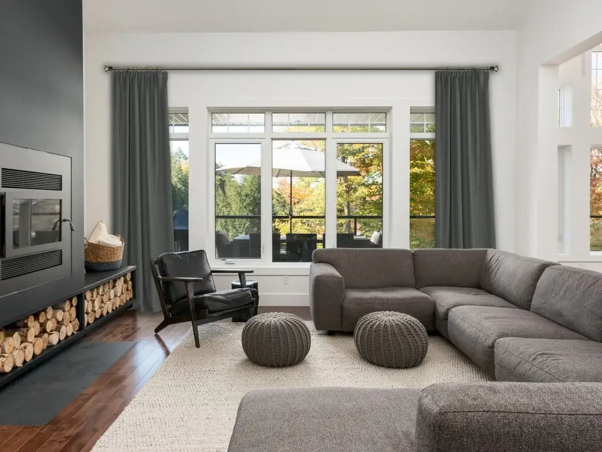 Nowoczesny salon z szarymi zasłonami i czarnym karniszem. Aranżacje okienne podkreślają przytulną atmosferę, a widok na jesienny ogr&oacute;d dodaje uroku.