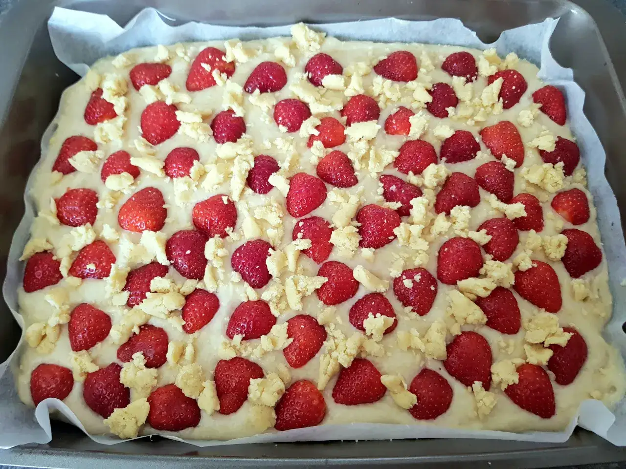 Ciasto widelcem mieszane z truskawkami i kruszonką, gotowe do pieczenia.