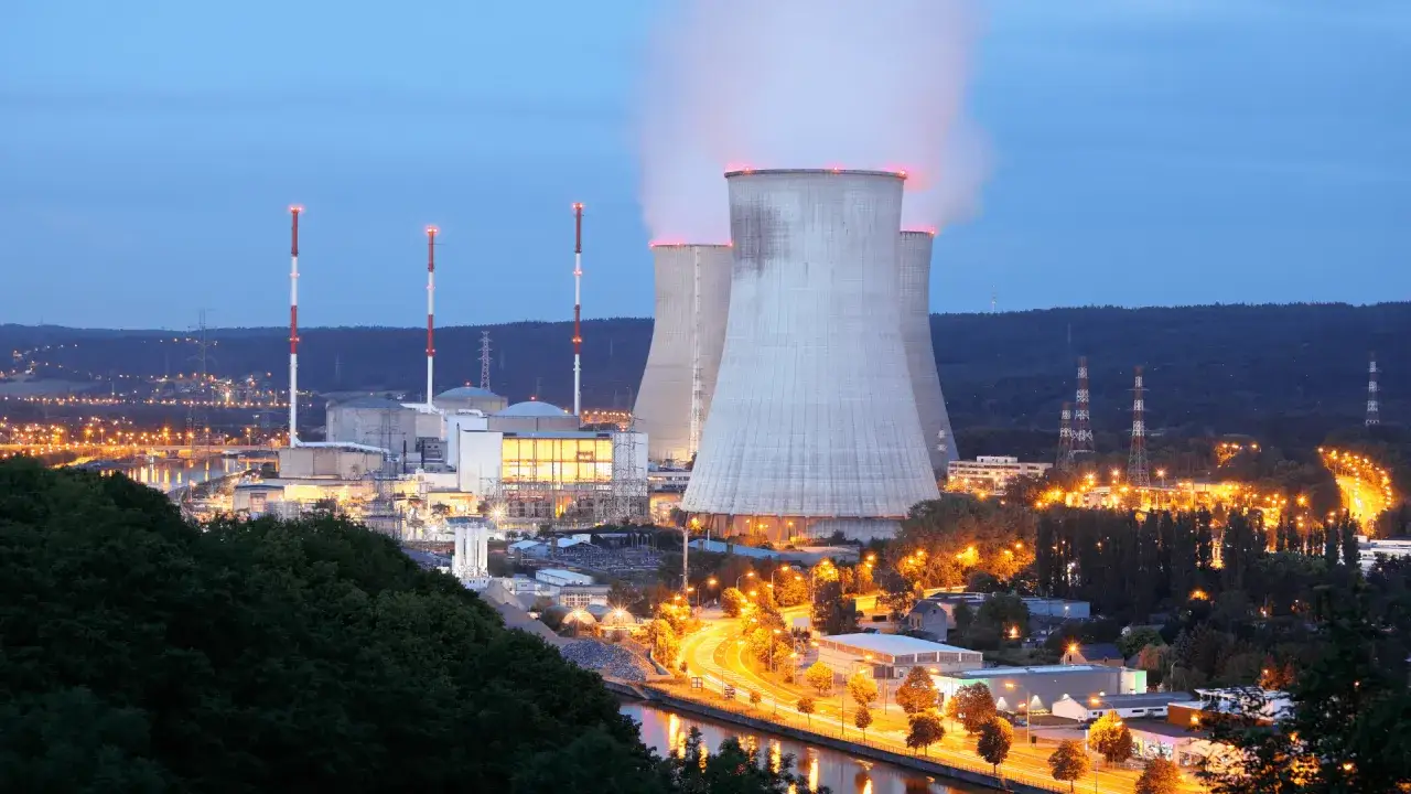 Elektrownia atomowa z chłodniami kominowymi i oświetlonymi budynkami. Zastanawiasz się, ile uranu zużywa elektrownia atomowa?