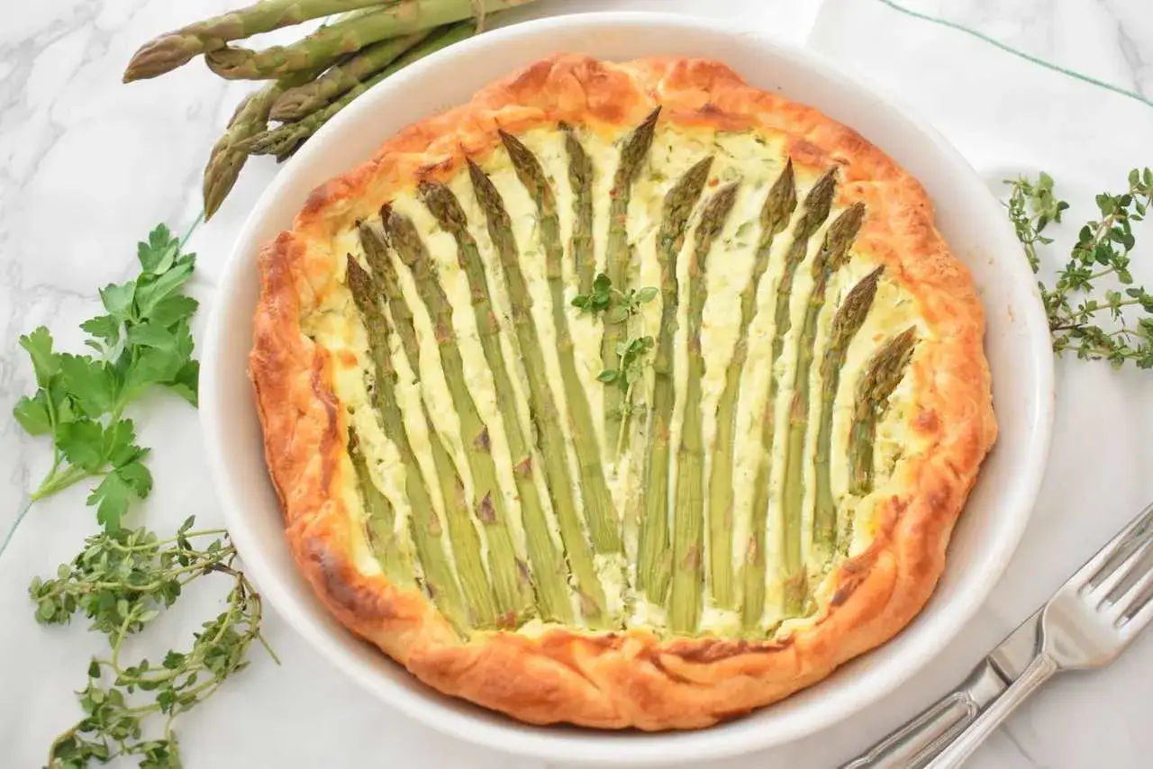 Apetyczna tarta ze szparagami, z chrupiącym ciastem i kremowym nadzieniem, ozdobiona świeżymi ziołami.