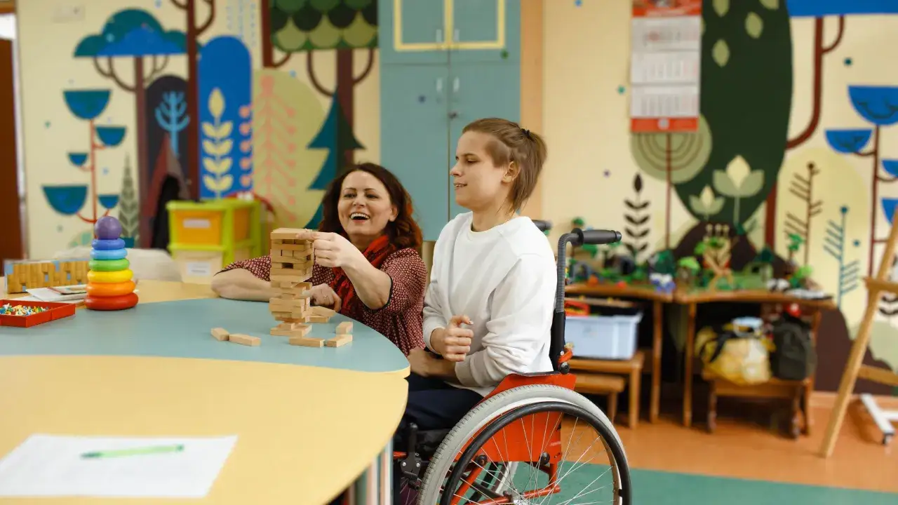 Kobieta i osoba na wózku grają w Jengę. To może być część zajęć w szkole policealnej, która oferuje wsparcie i rozwój.