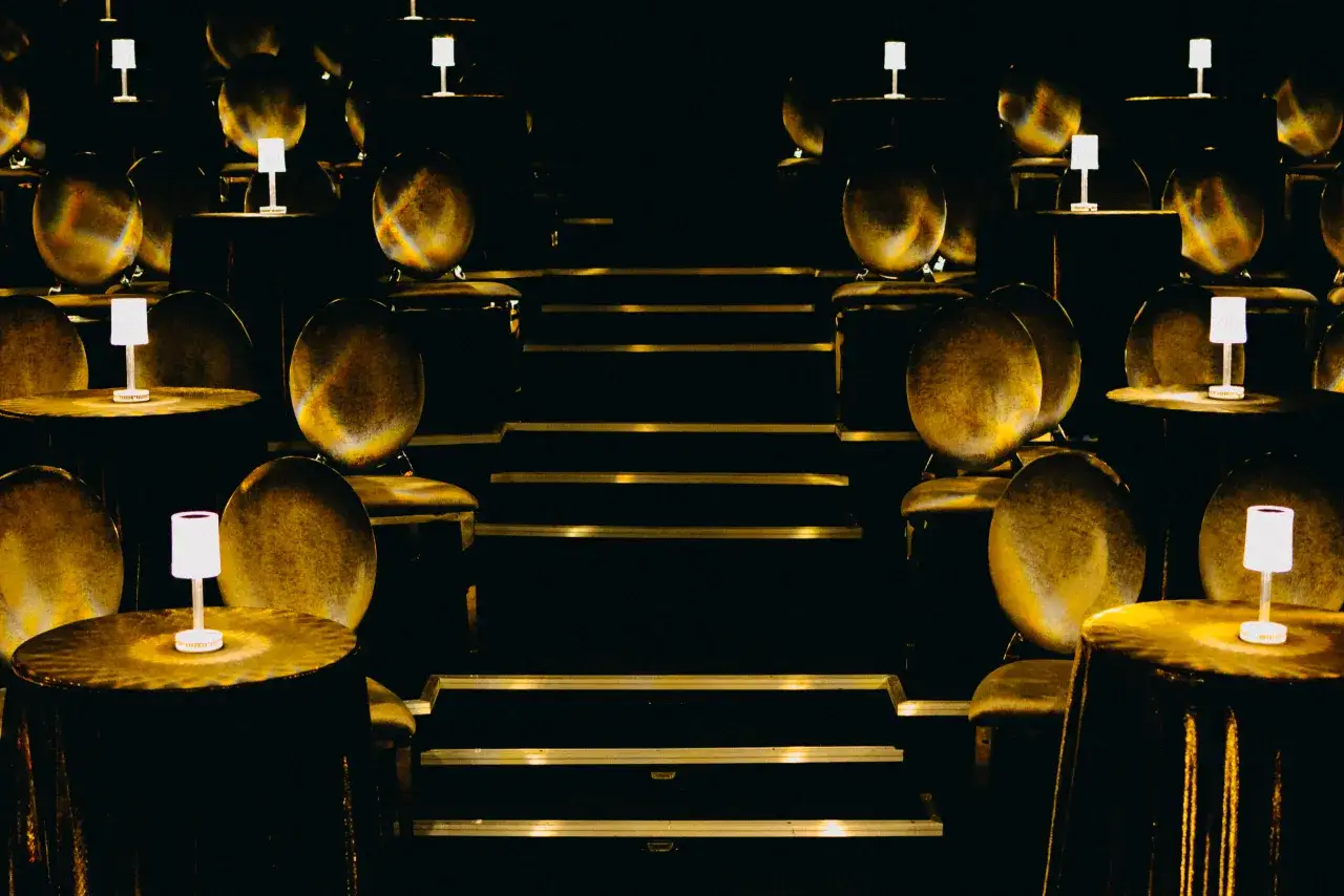 Wnętrze teatru w Warszawie, z rzędami złotych kul i stolik&oacute;w z lampkami.