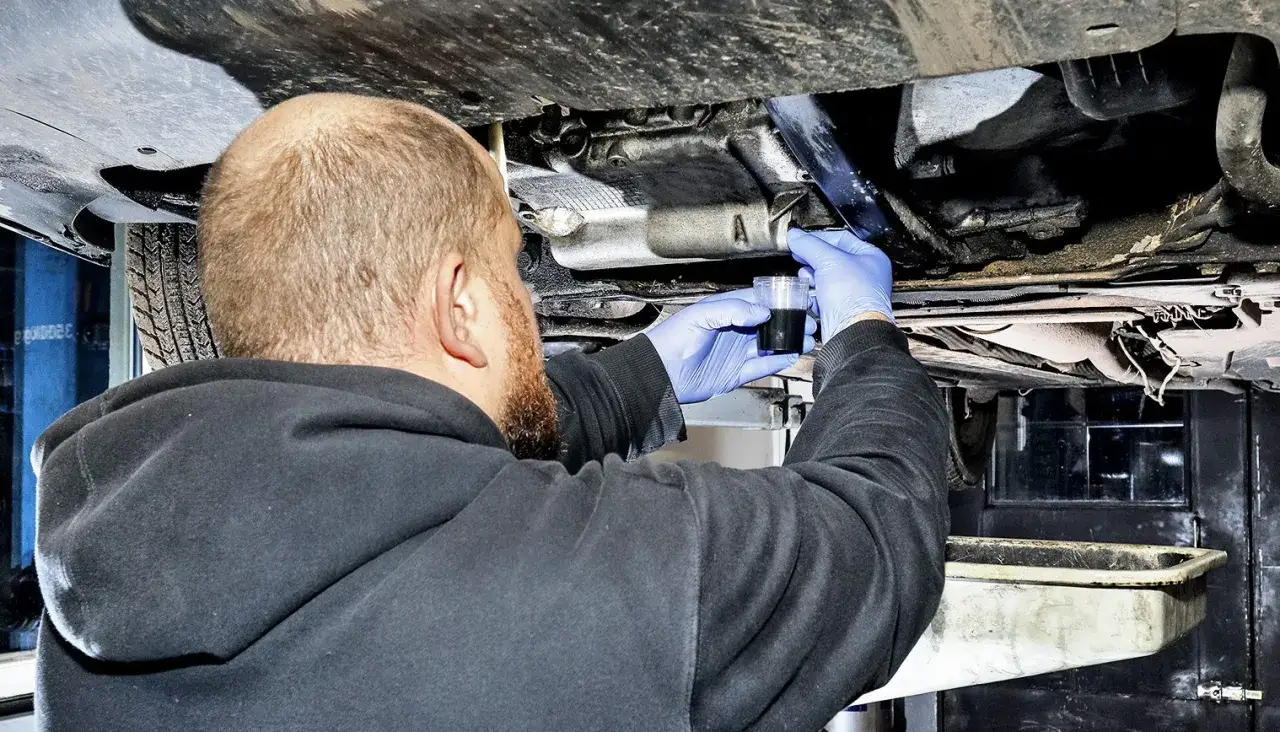 Mechanik w niebieskich rękawiczkach sprawdza płyn po płukaniu silnika przed wymianą oleju.
