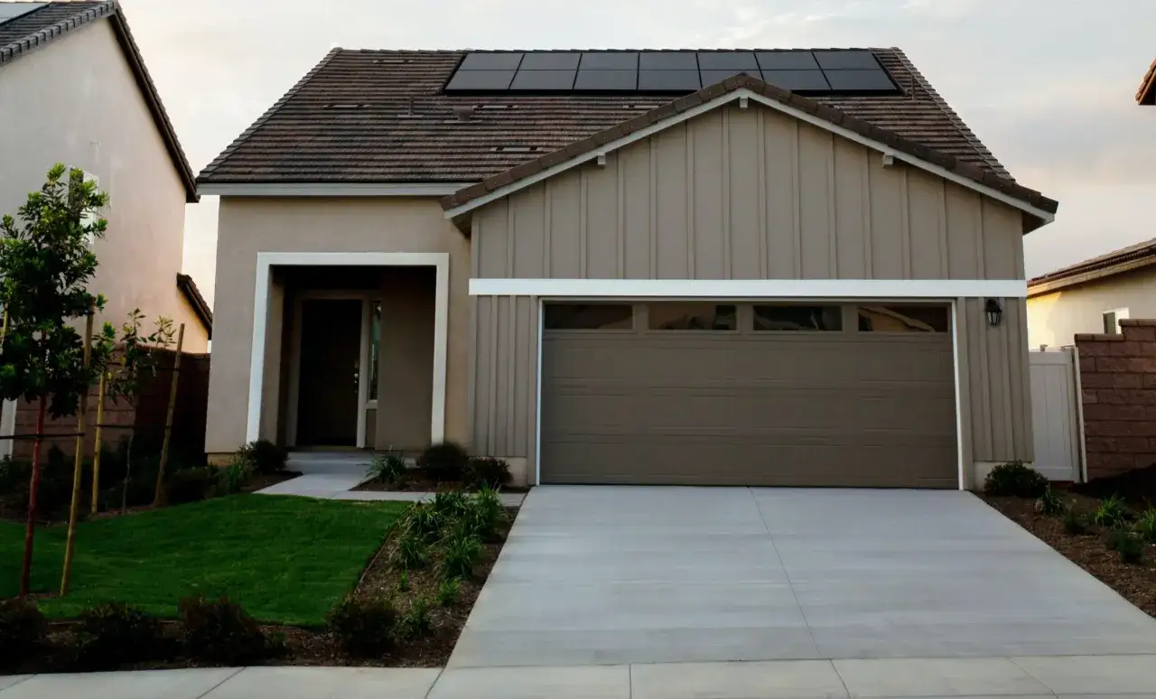Nowoczesny dom z panelami słonecznymi na dachu i brązową bramą garażową. Zastanawiasz się, ile kosztuje wynajem garażu w tej okolicy?