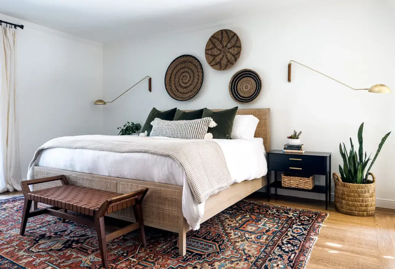 Przytulna sypialnia w stylu hiszpańskim z plecionymi koszami na ścianie, ł&oacute;żkiem z rattanowym zagł&oacute;wkiem i orientalnym dywanem.