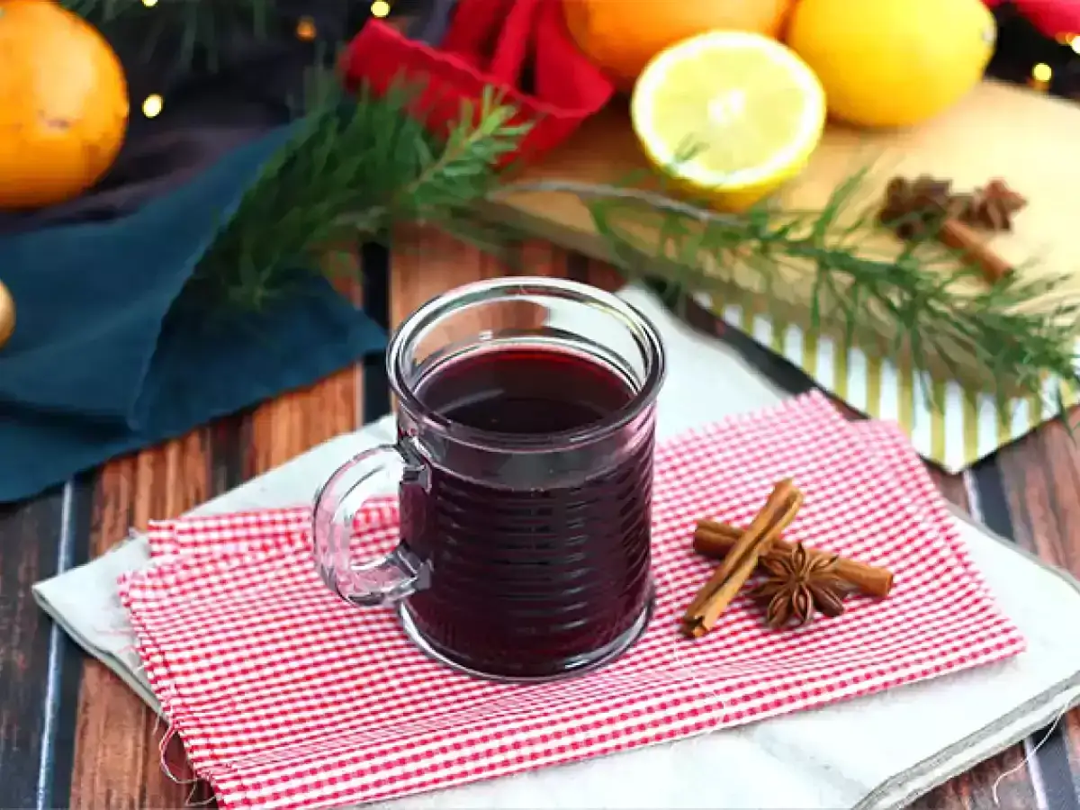 Kubek grzanego wina z przyprawami: cynamonem i anyżem. Obok pomarańcze, cytryna i gałązka świerku.