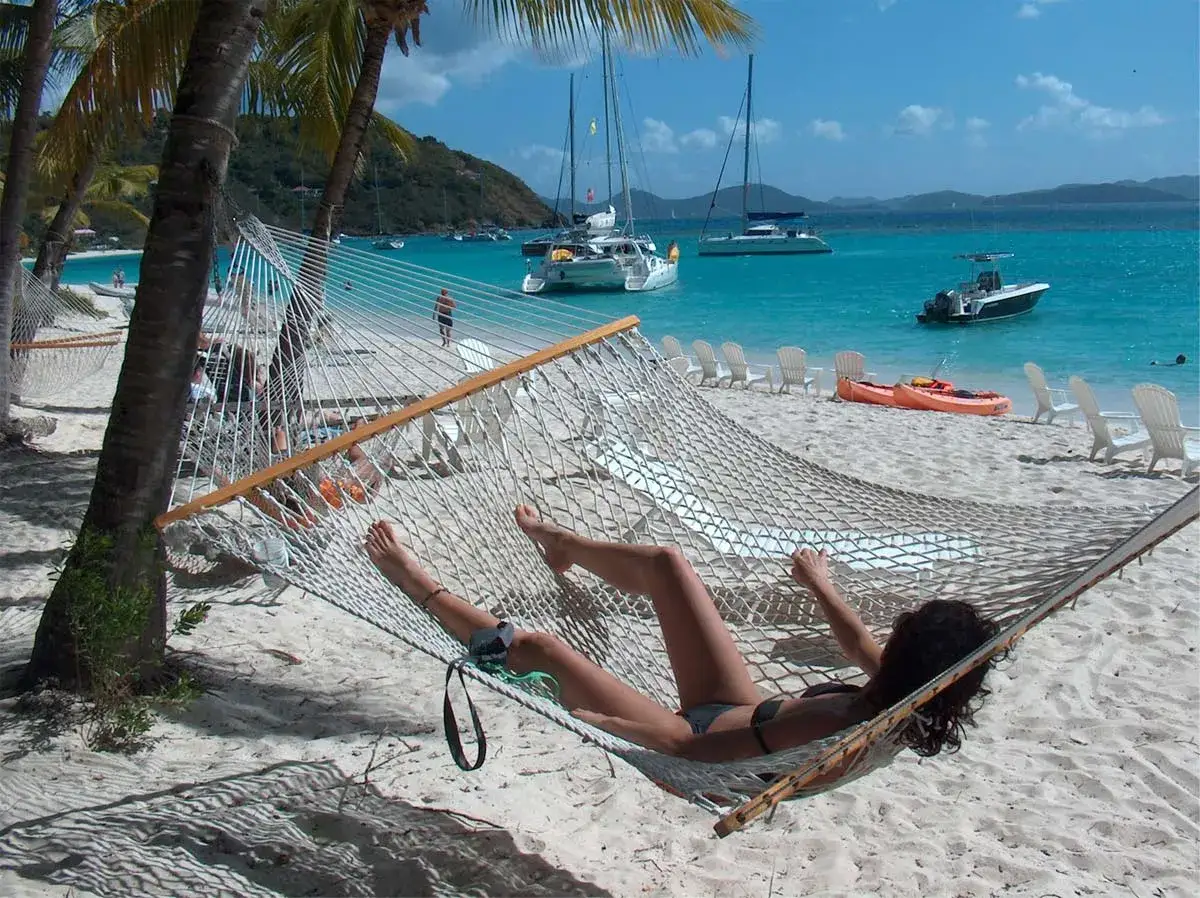 Relaks na plaży, idealny moment, by poczuć klimat Karaibów. W tle błękitne morze, łodzie i palmy.
