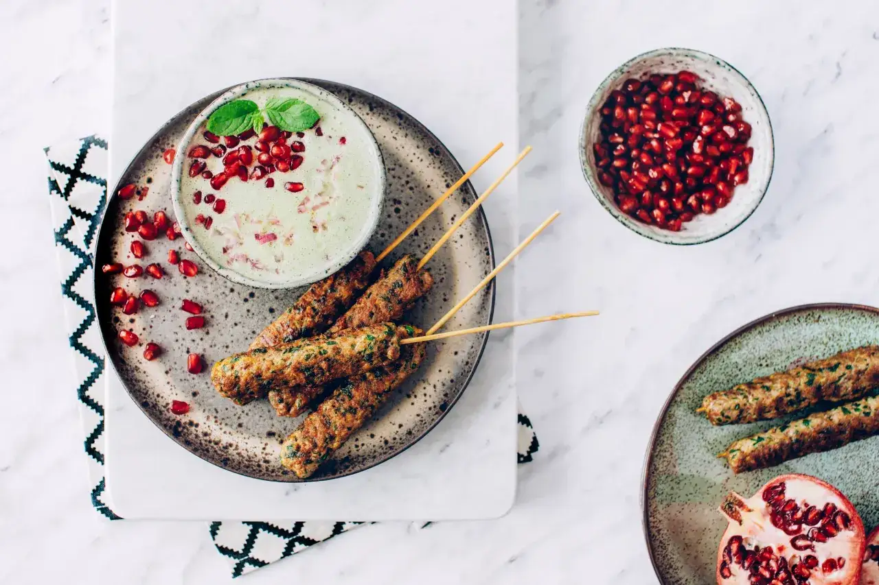 Kebab na patykach z kremowym sosem miętowym do kebaba, ozdobionym granatem i listkami mięty.