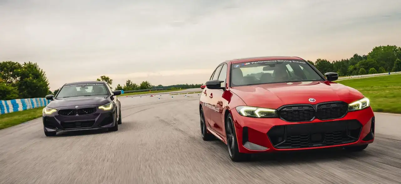 Dwa BMW M3 G80, czerwone i fioletowe, ścigają się na torze wyścigowym podczas szkolenia BMW Performance Driving School.