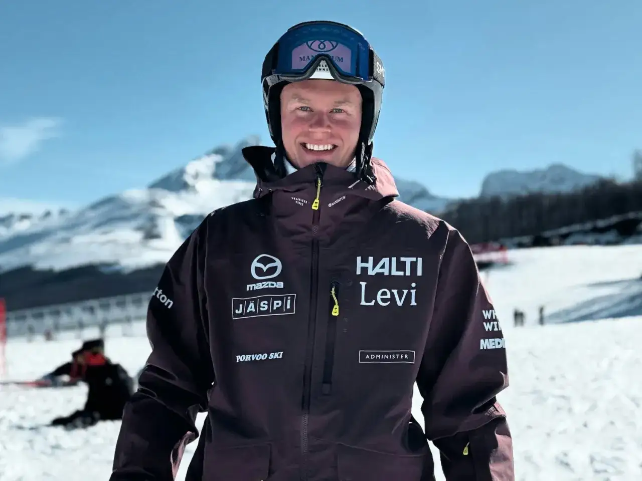 Uśmiechnięty narciarz w kurtce Halti Levi, z logo Mazda i innymi sponsorami. Firma Halti to znany producent odzieży sportowej.