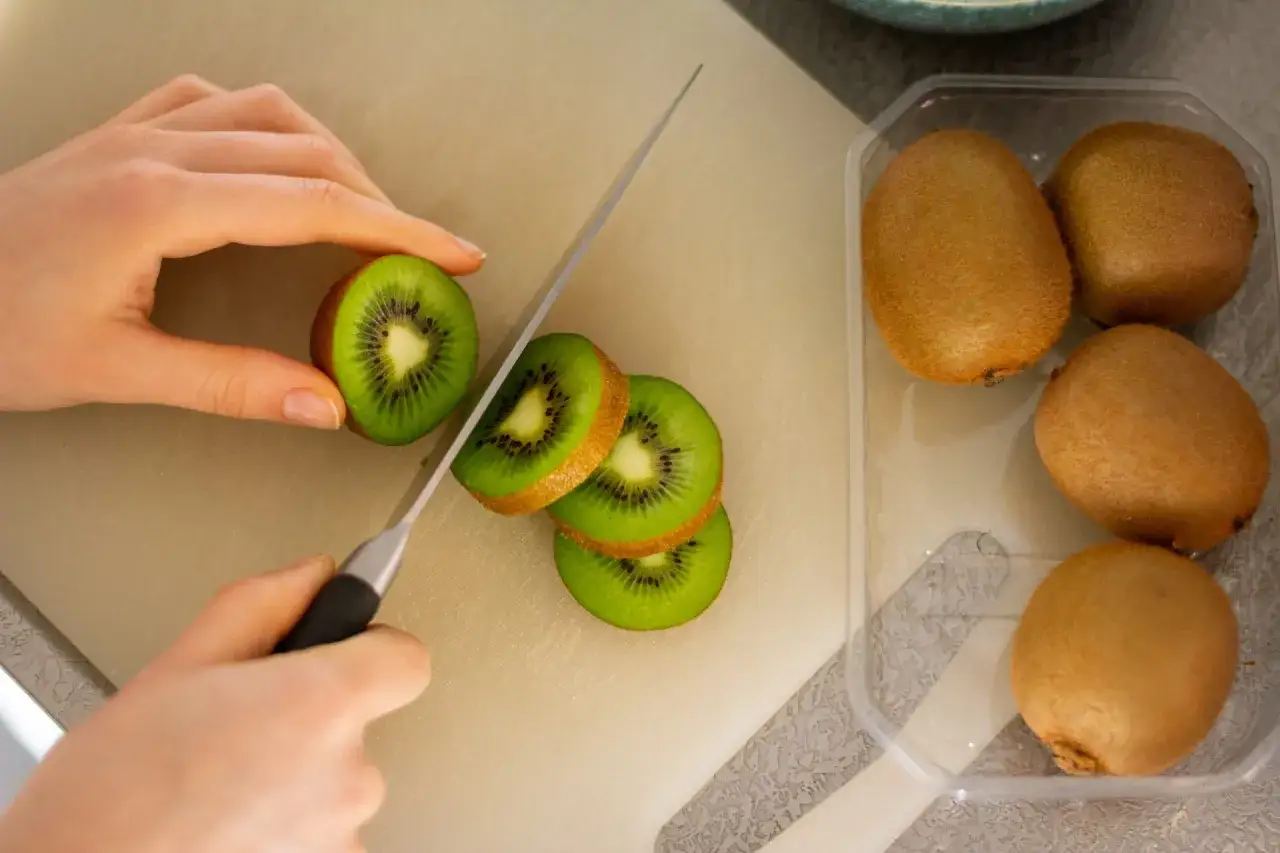 Krojenie kiwi na desce. Uważaj na skutki uboczne jedzenia kiwi, takie jak alergie.