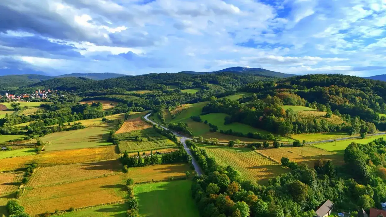 Malowniczy krajobraz Beskidu Kłodzko z polami, lasami i drogą wijącą się wśr&oacute;d zieleni.