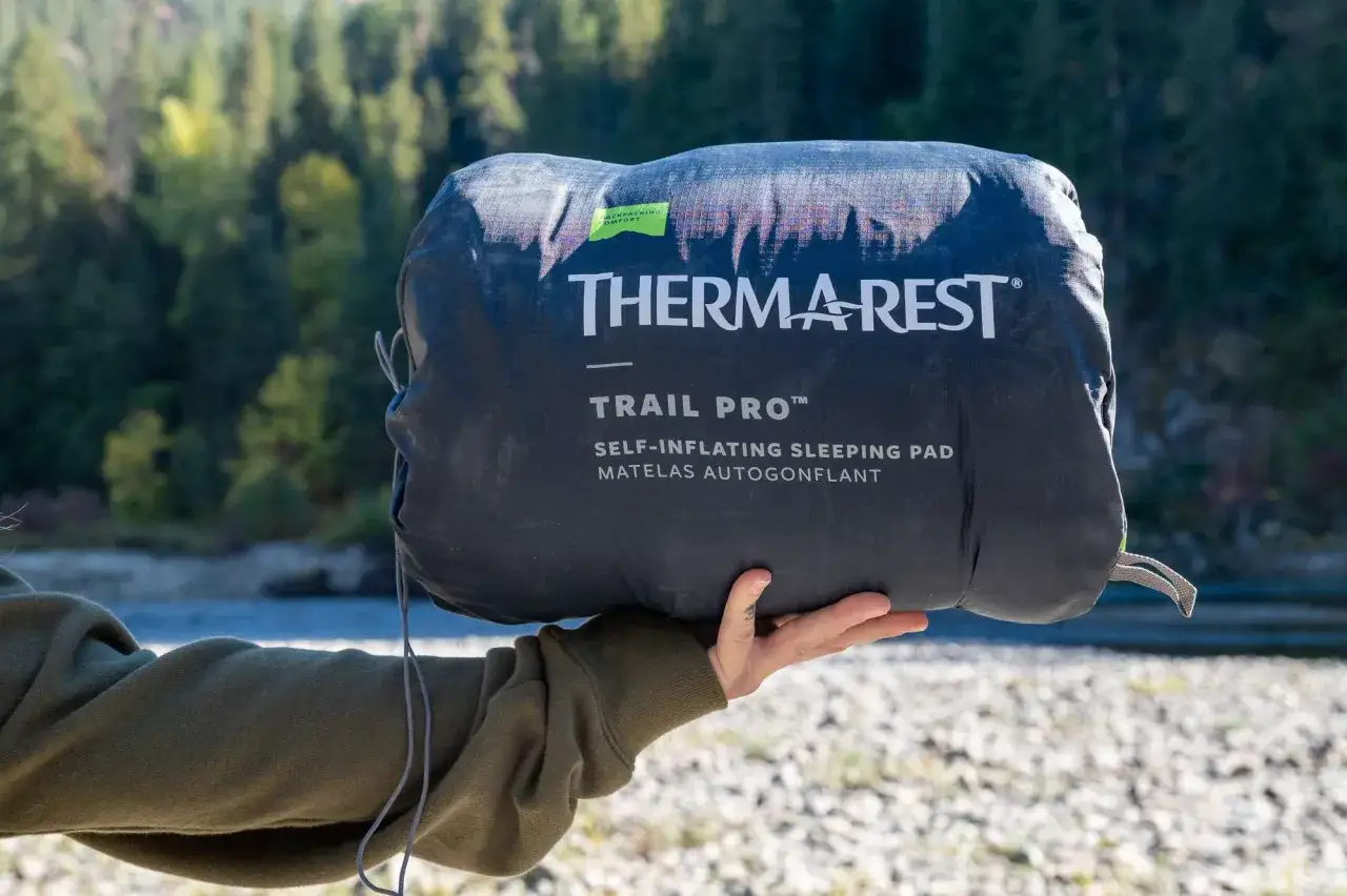Ręka trzyma zwinięty materac samopompujący Therm-a-Rest Trail Pro. Niezbędne gadżety pod namiot na wyprawę.