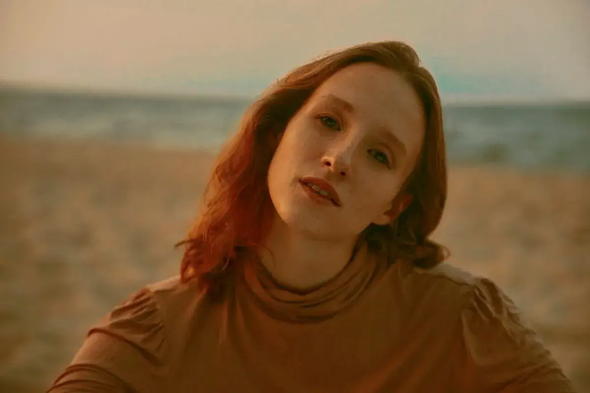 Anna Paliga z rudymi włosami i piegami na twarzy, na tle plaży i morza.