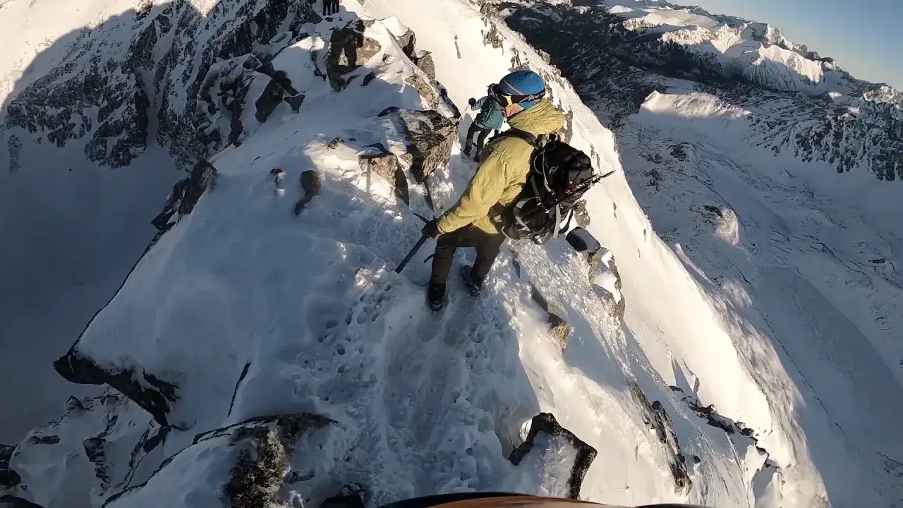 Wspinacze naśnieżnym grzbietem, pokonując trudne szlaki. W tle majestatyczne góry.