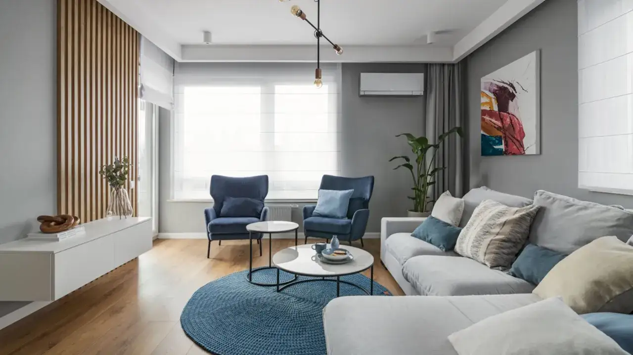 Nowoczesny salon z granatowymi fotelami i szarą sofą. Inspiracje szare ściany podkreślają drewniane lamele i abstrakcyjny obraz.