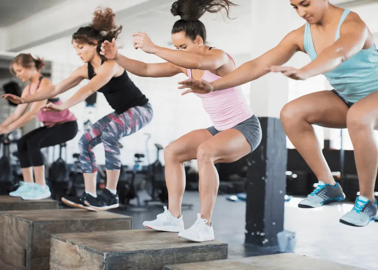 Kobiety wykonują ćwiczenia plyometryczne na skrzyniach. Brak kondycji objawy mogą ustąpić dzięki takim treningom.