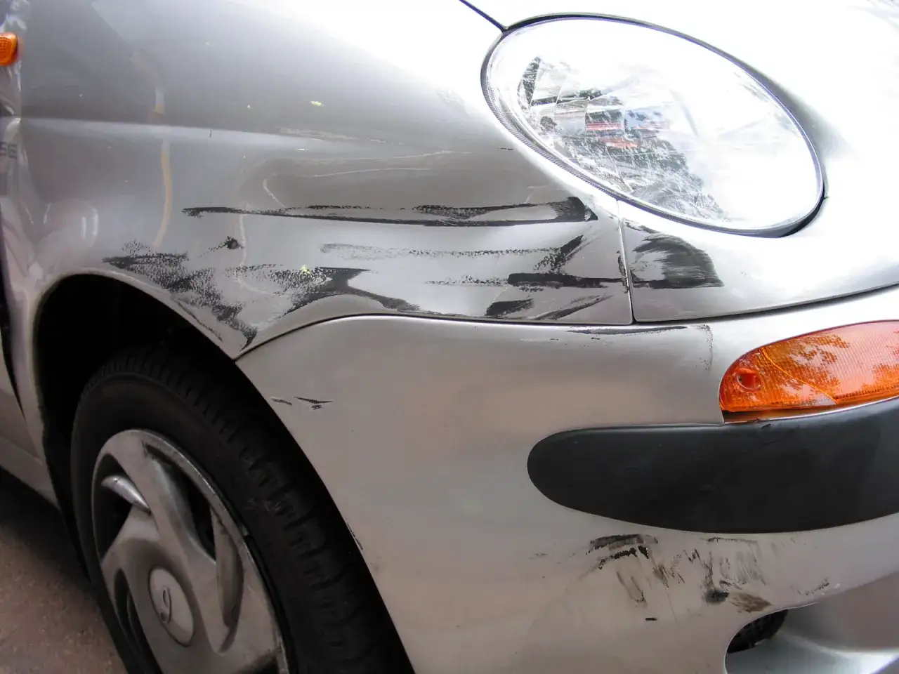 Srebrne auto z licznymi głębokimi rysami i wgnieceniami na błotniku i zderzaku. Zastanawiasz się, jak usunąć rysy z auta?