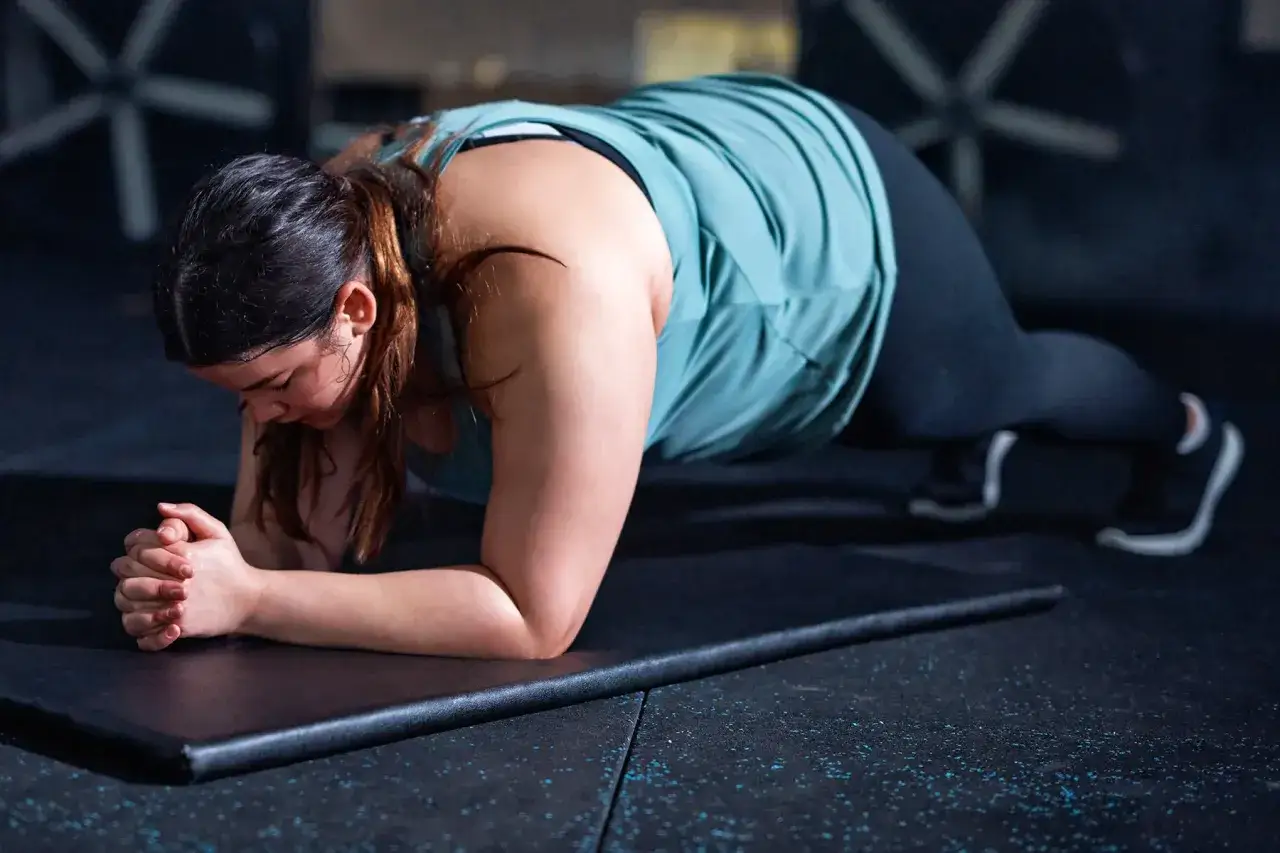 Kobieta wykonuje plank, jedno z ćwiczeń na schudnięcie z brzucha, skupiona na treningu w siłowni.