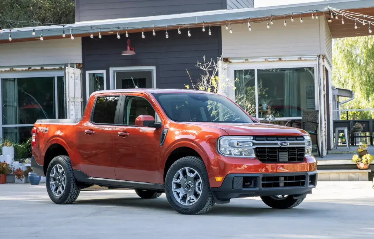 Pomarańczowy Ford Maverick z napędem FX4 stoi przed nowoczesnym domem z girlandą światełek.
