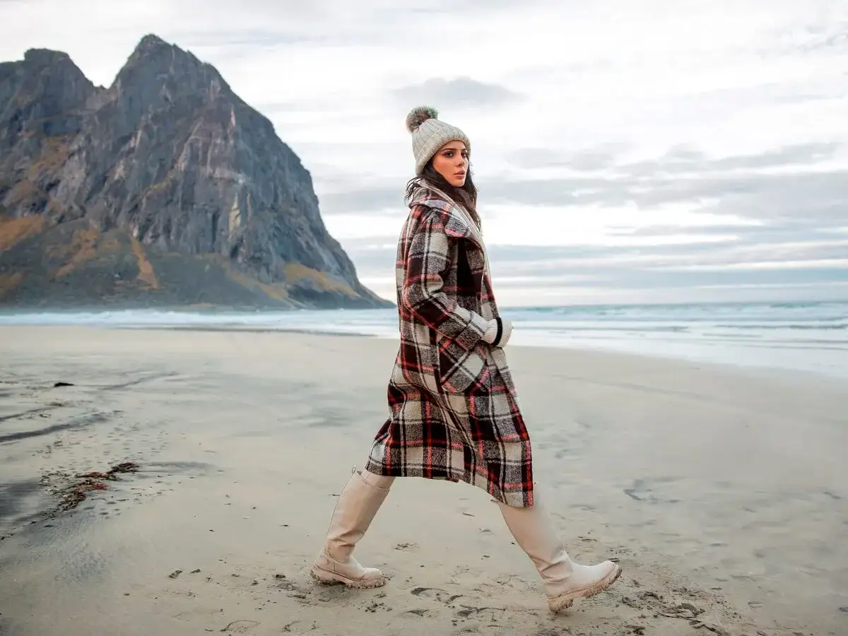 Kobieta w stylowych płaszczach damskich w kratkę spaceruje po plaży, w tle majestatyczna góra.