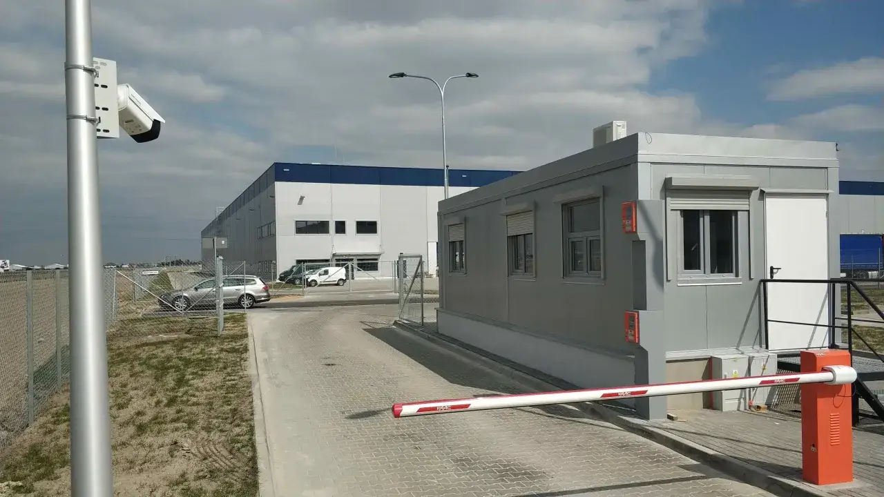 System rozpoznawania tablic rejestracyjnych monitoruje wjazd na teren obiektu przemysłowego. Kamera rejestruje pojazdy, a szlaban czeka na autoryzację.