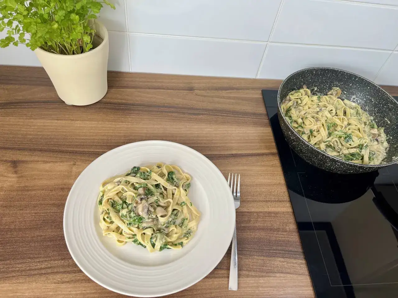 Porcja tagliatelle ze szpinakiem i grzybami na talerzu. W garnku widać resztę dania. Idealna ilość makaronu tagliatelle na osobę.