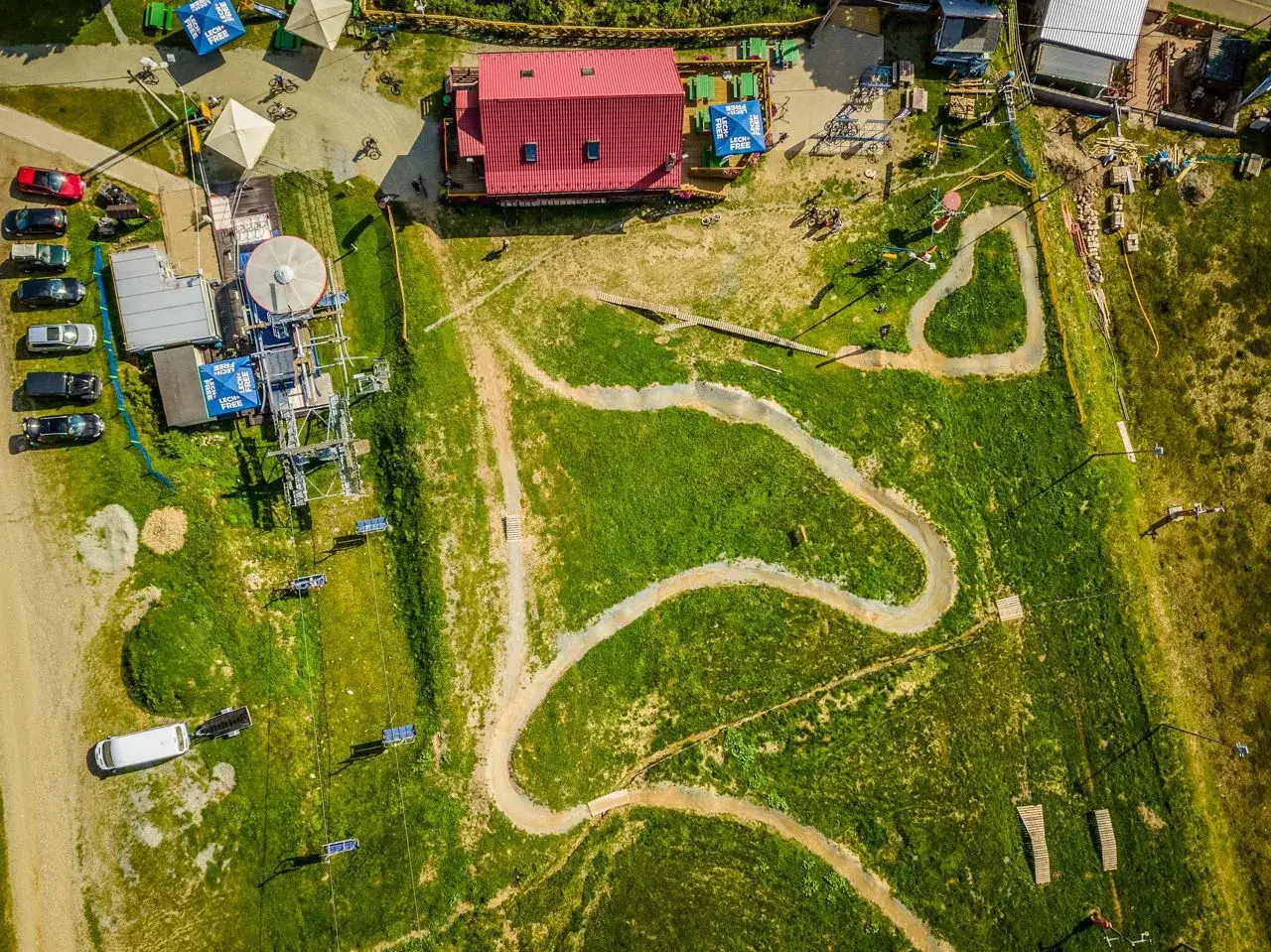 Widok z lotu ptaka na zieleniec bike park z wyciągiem krzesełkowym, torem rowerowym i budynkiem z czerwoną dachem.