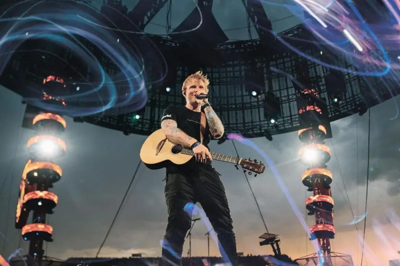 Ed Sheeran śpiewa i gra na gitarze na scenie, otoczony efektami świetlnymi. Marzenie o koncercie Eda Sheerana w Polsce staje się rzeczywistością!