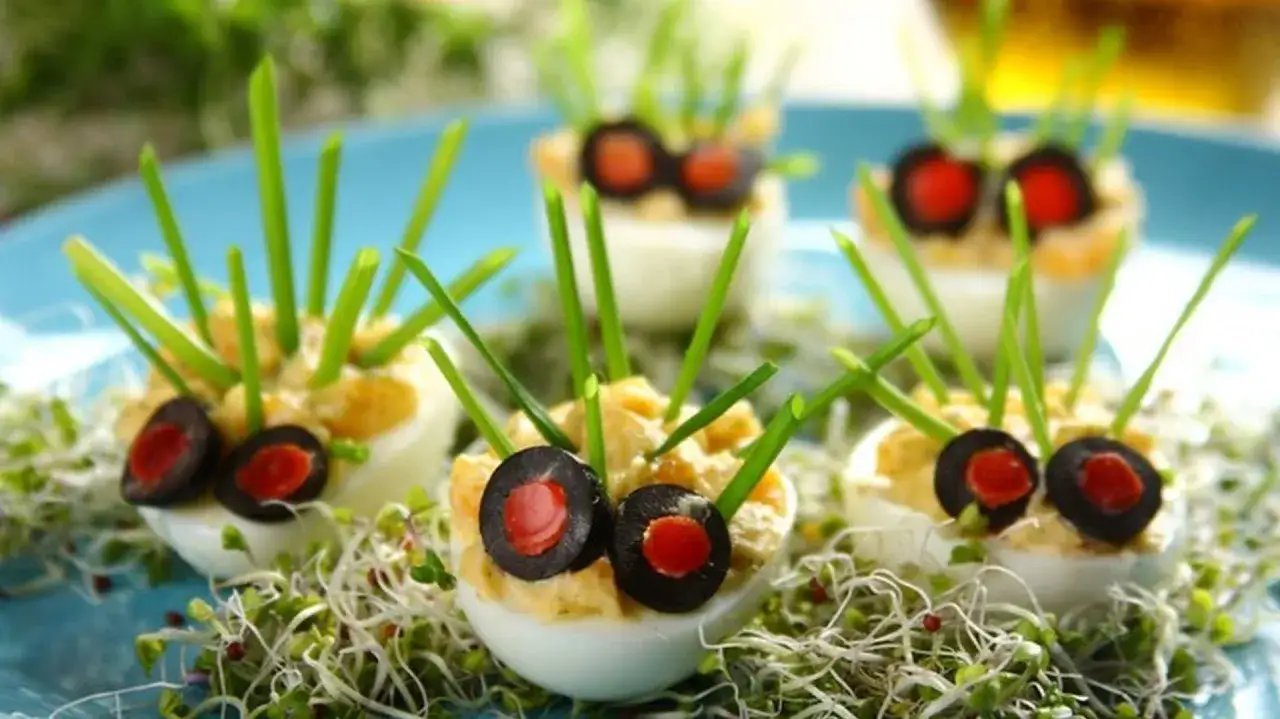 Urocze jajka faszerowane, ozdobione jak jeżyki z oliwek i szczypiorku. Idealne do wypr&oacute;bowania w ramach 14 przepis&oacute;w na jajka faszerowane.