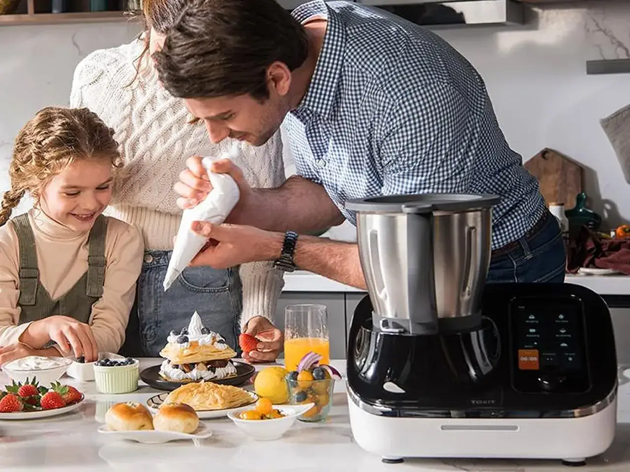 Rodzina przygotowuje deser. Ojciec z córką dekorują ciasto, obok stoi nowoczesny robot kuchenny, który może pomóc w wyborze, jaki air fryer wybrać.